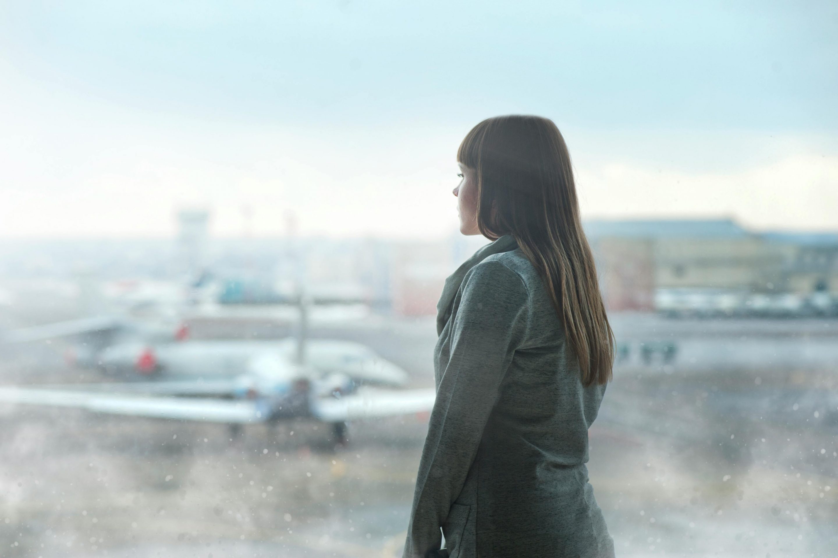 A woman looks through an airport window at a row of planes